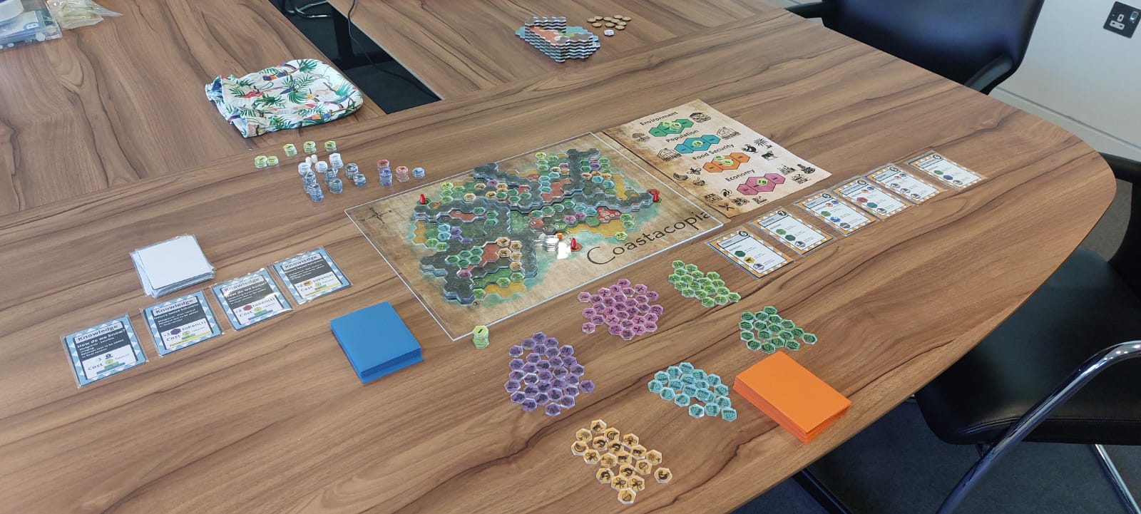 A board game arranged on a tabletop with adjacent chairs, inviting players to join in the game.