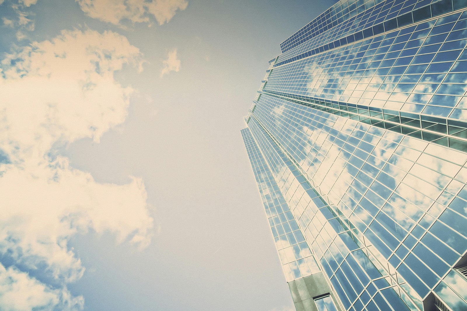 A towering building rises against a clear blue sky, with scattered white clouds.
