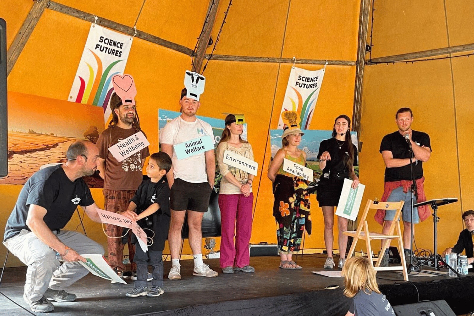 Participants on stage displaying signs that address various food challenges, inviting the audience to discuss food system strategies.