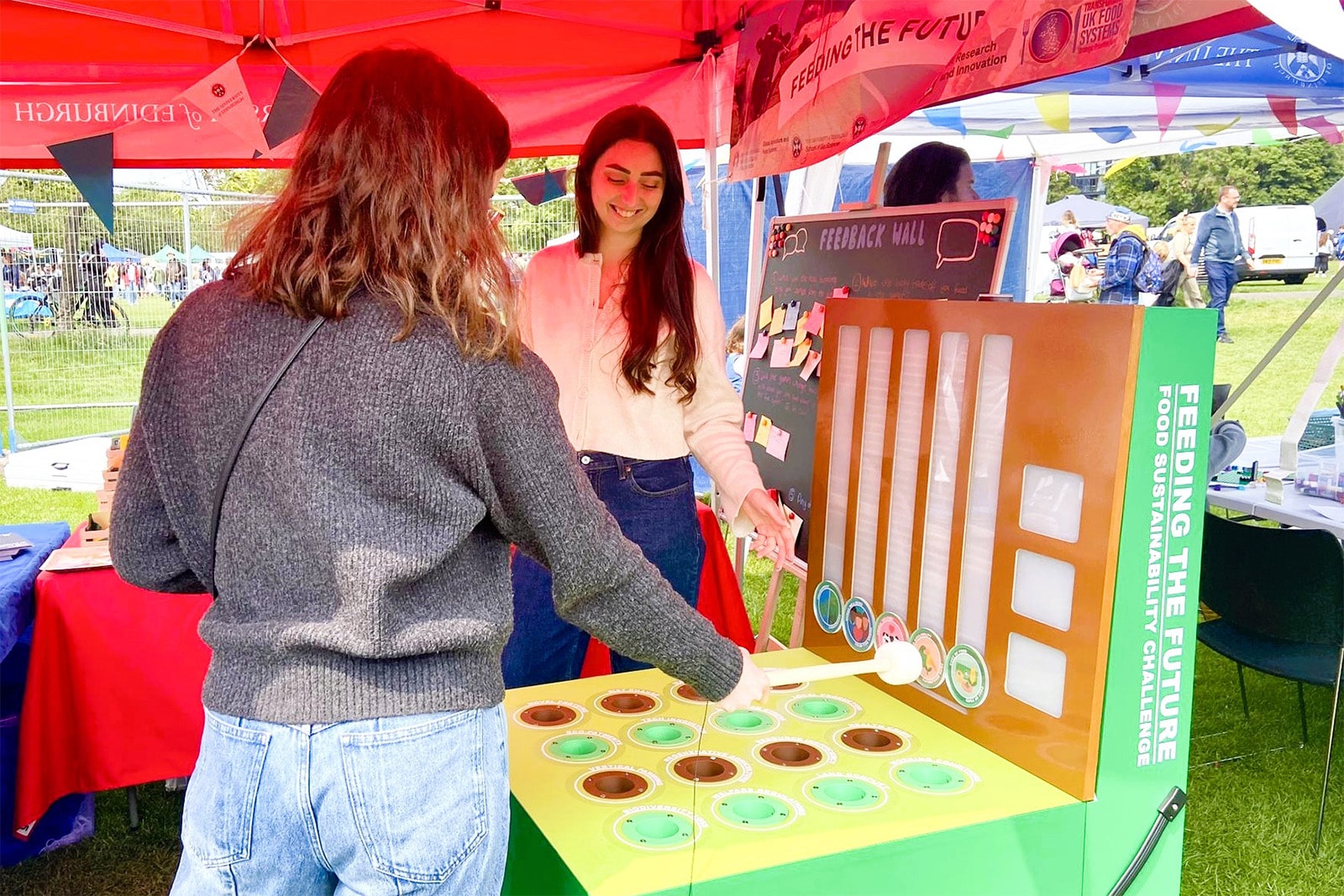Project lead, Kirsty Blair demonstrates to another person how to play the Whac-a-Mole-inspired food sustainability challenge.