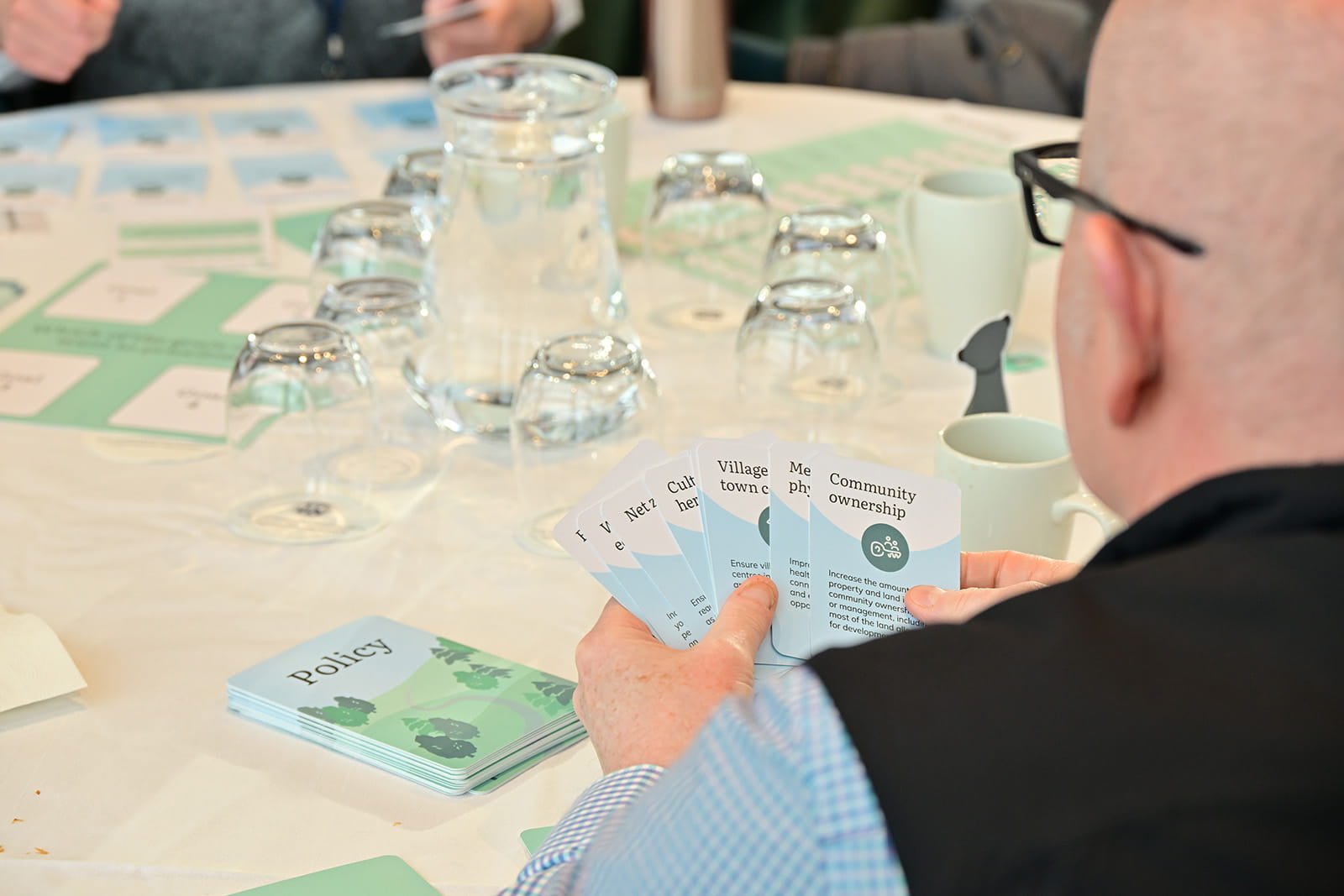 A man participating in the Otter Power card game, with several other players at a table