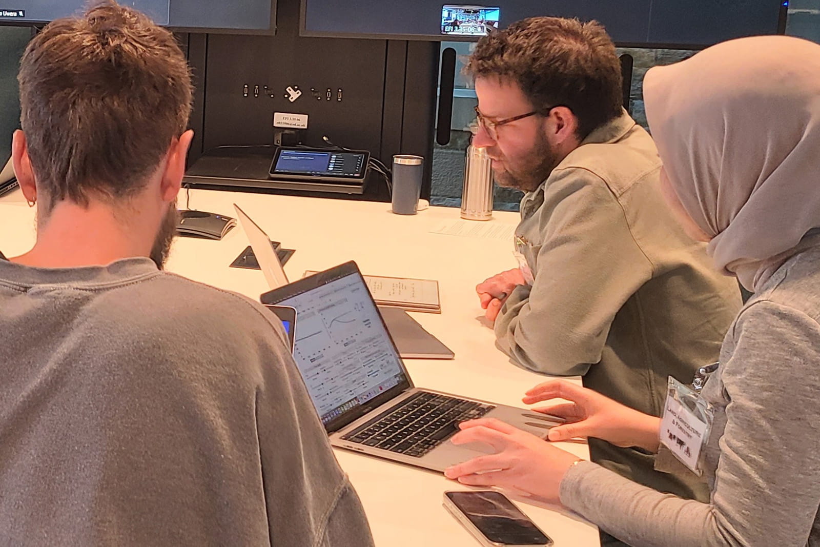 Three individuals seated at a table, each using a laptop, engaged in a collaborative work session.