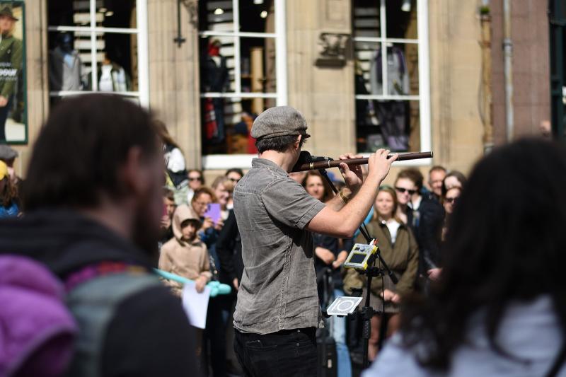 A musician performs on the flute for an attentive audience at the Edinburgh Festival Fringe, creating a lively atmosphere.  