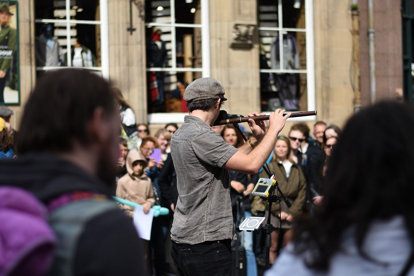A musician performs on the flute for an attentive audience at the Edinburgh Festival Fringe, creating a lively atmosphere.  